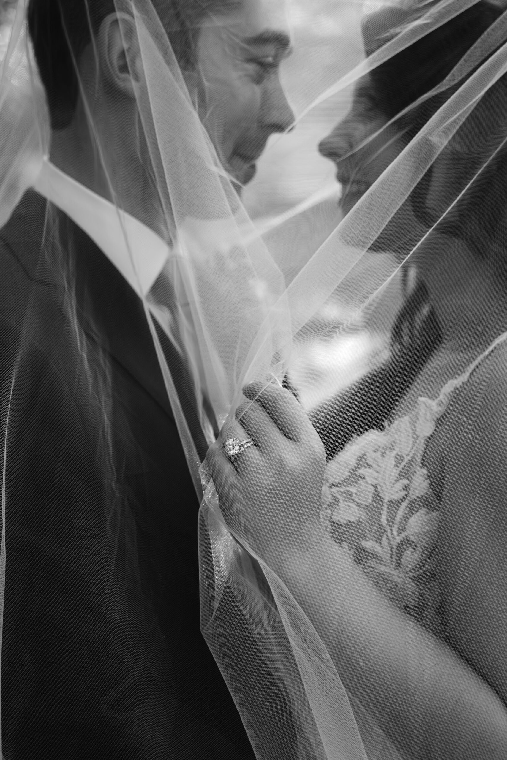 bride and groom underneath veil on wedding day with engagement ring